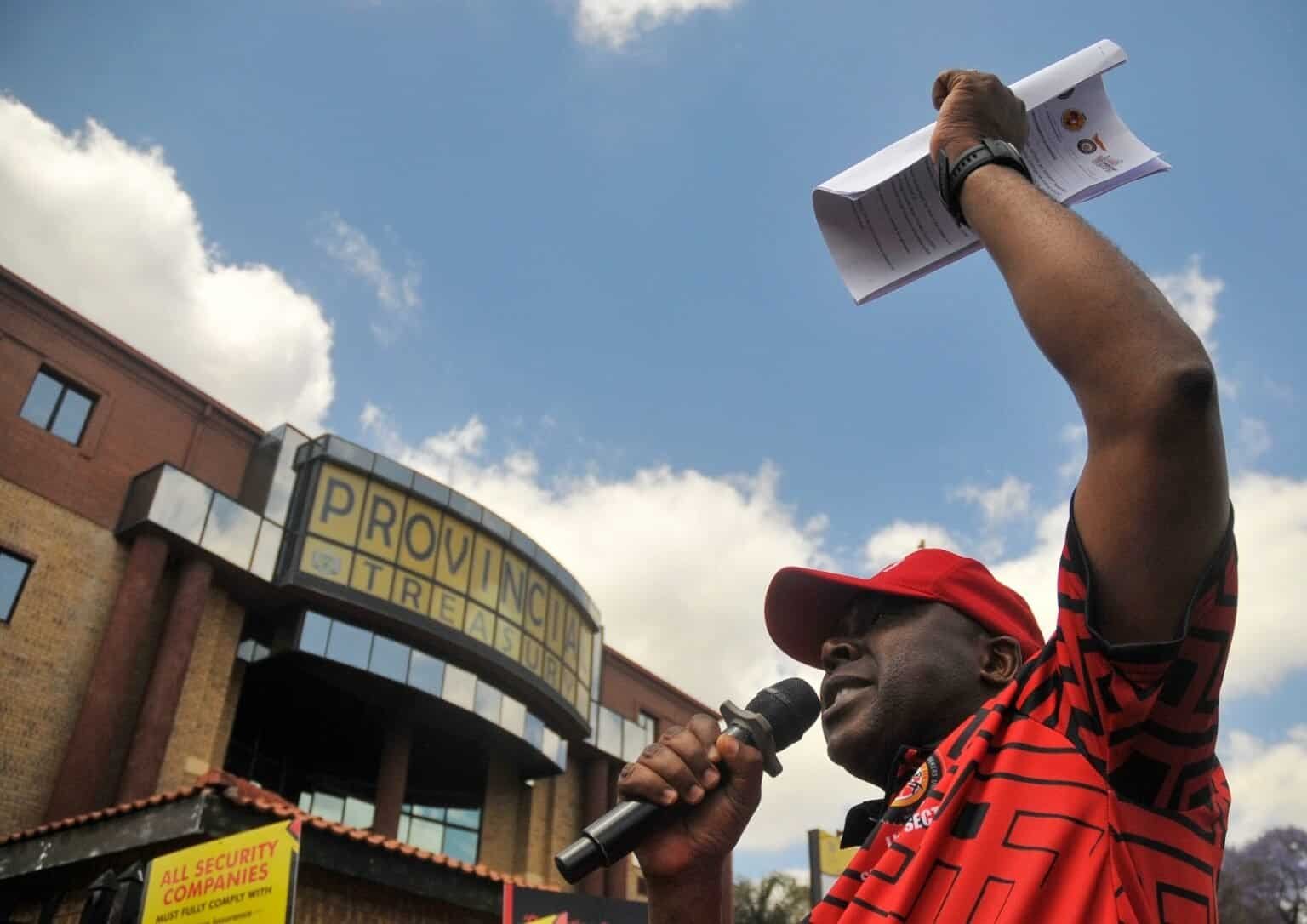 Protester speaking with microphone outside Provincial Treasury building, advocating for economic or political change in Africa.