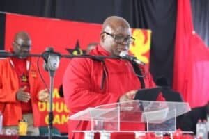 Provincial Secretary Chuene Malebana speaking at a political event in South Africa, wearing red vest with SACP logo.