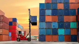 A red forklift moves containers in a busy shipping yard during sunset for logistics and trade.
