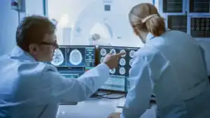 Medical researchers examining brain scans on multiple monitors in a lab.