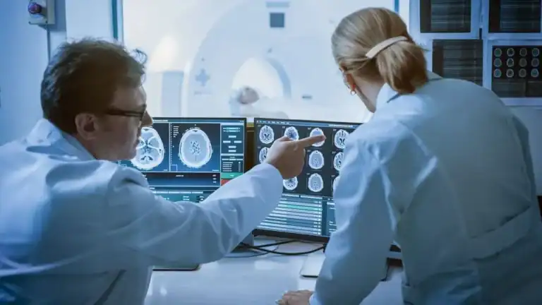 Medical researchers examining brain scans on multiple monitors in a lab.