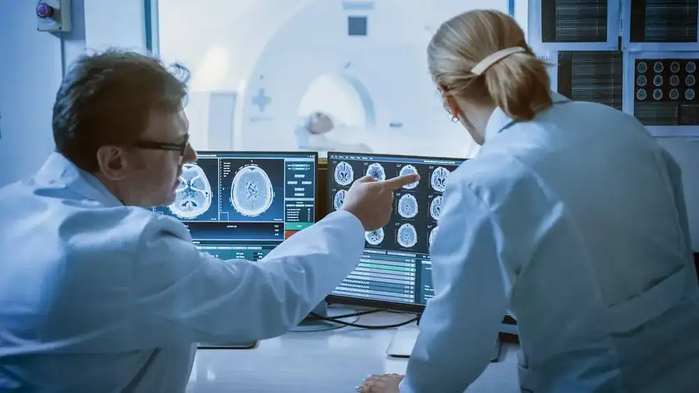 Medical researchers examining brain scans on multiple monitors in a lab.