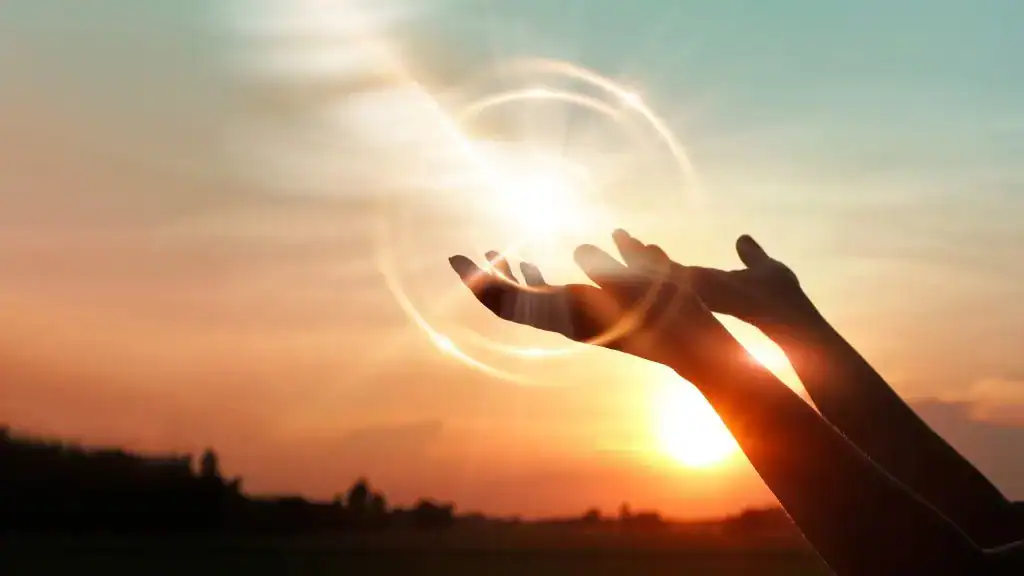 Hand reaching towards the sunset with a glowing sun and vibrant sky.