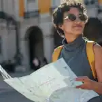 Woman with sunglasses holding a map in a city square, ready to explore.