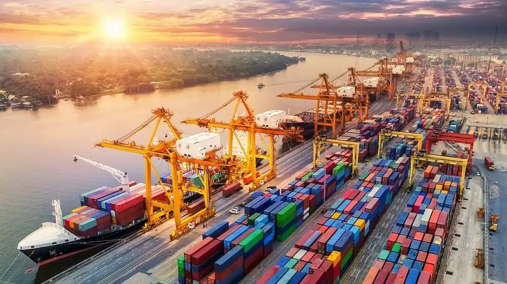 Port cargo and container terminal with cranes and shipping containers at sunset.