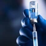 Egypt Aims to Produce 140 Million Vaccine Doses Annually by 2030. Healthcare professional administering COVID-19 vaccine with syringe.