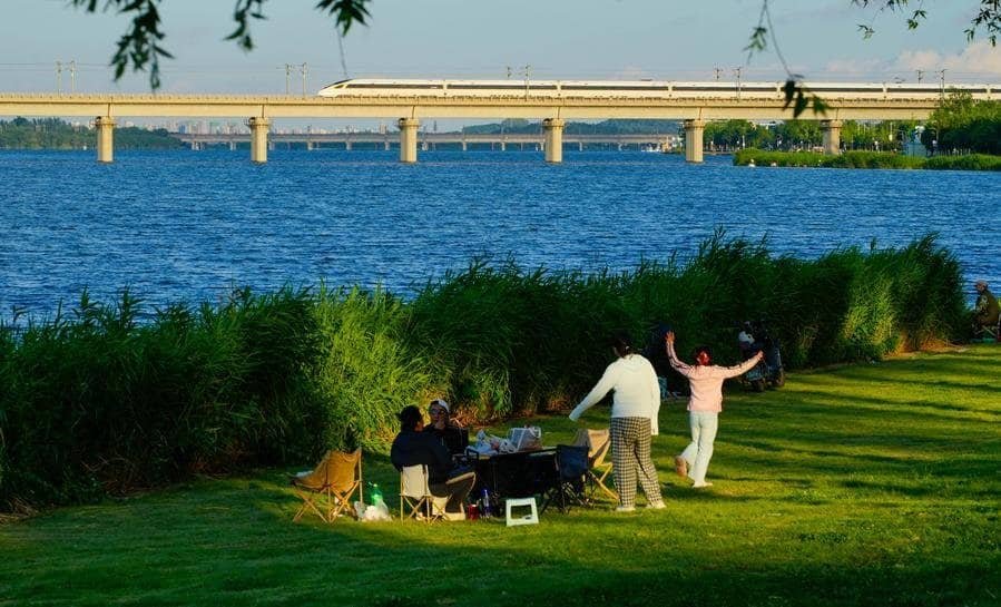 People enjoy leisure time by the Hutuo River as a bullet train runs on a bridge in distance in Shijiazhuang City, north China's Hebei Province, June 8, 2026. (Photo by Yan Zhiguo/Xinhua)