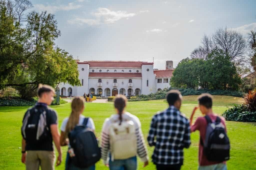 Students walking towards a historic school building on a sunny day.