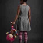 Young girl with curly hair in a gray dress holding a colorful doll.