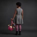 Young girl with curly hair in a gray dress holding a colorful doll.