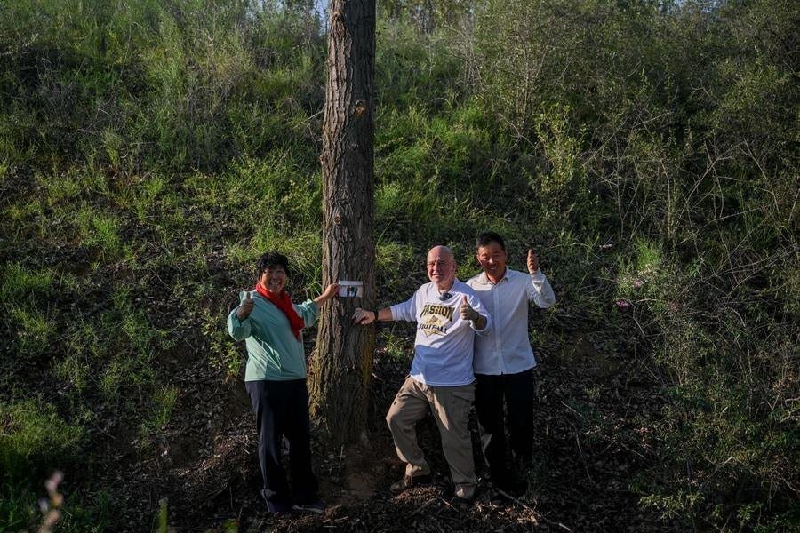 Yin Yuzhen (L), Bai Wanxiang (R) and Ronald Sakolsky pose for a photo with a tree they once planted together in the Maowusu Sandy Land in north China's Inner Mongolia Autonomous Region, Aug. 24, 2026. (Xinhua/Lian Zhen)
